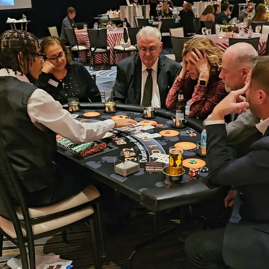 A uniformed dealer deals cards to guests around a blackjack table at an indoor event.