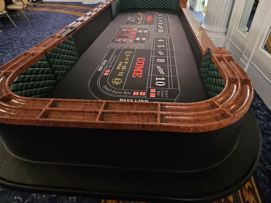 A wood-trimmed craps table with a black betting layout in an indoor venue.