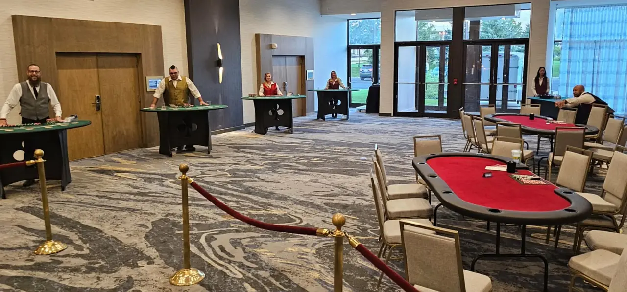 Uniformed casino-party dealers stand behind tables in an event room.